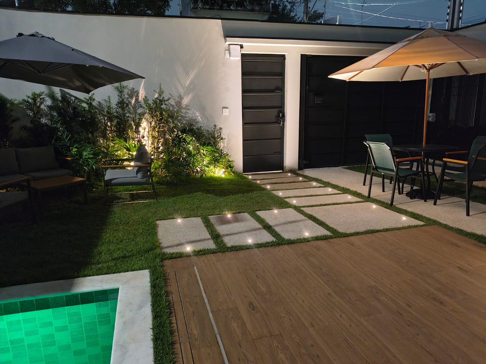 Área externa à noite com piscina iluminada, ombrelones e lounges