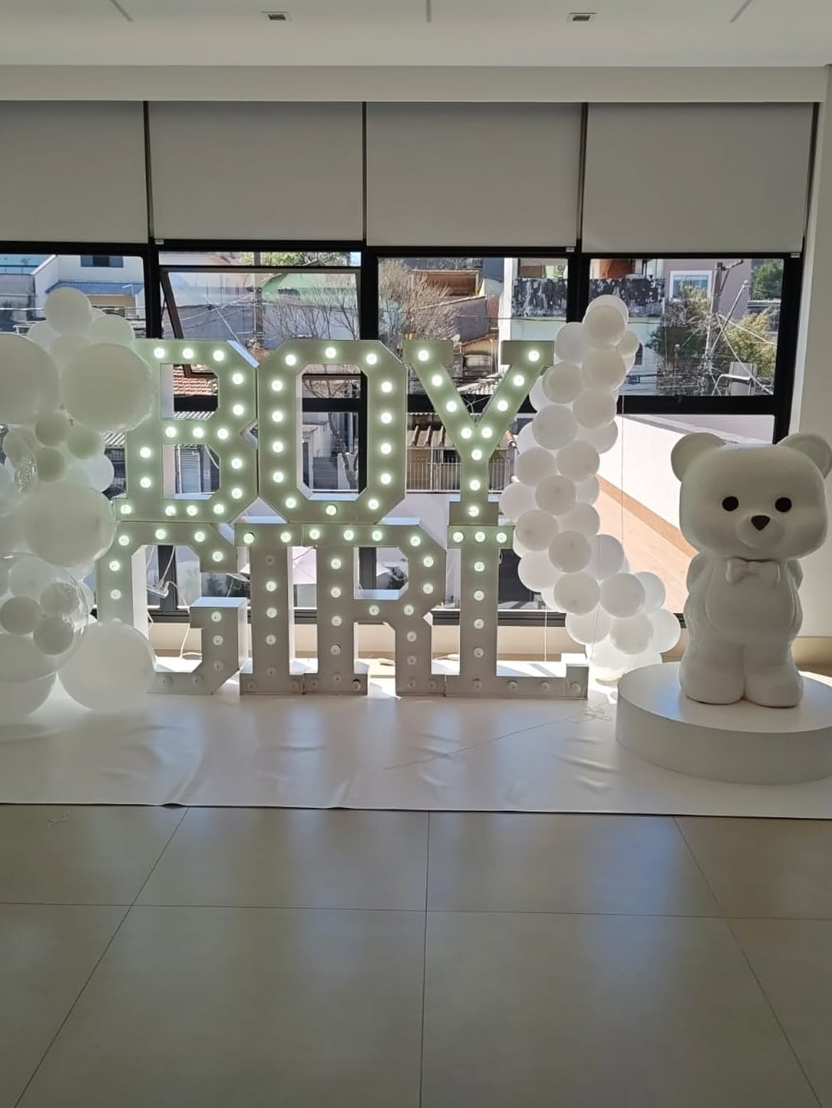 Letreiro luminoso Boy or Girl com balões brancos e urso decorativo no salão