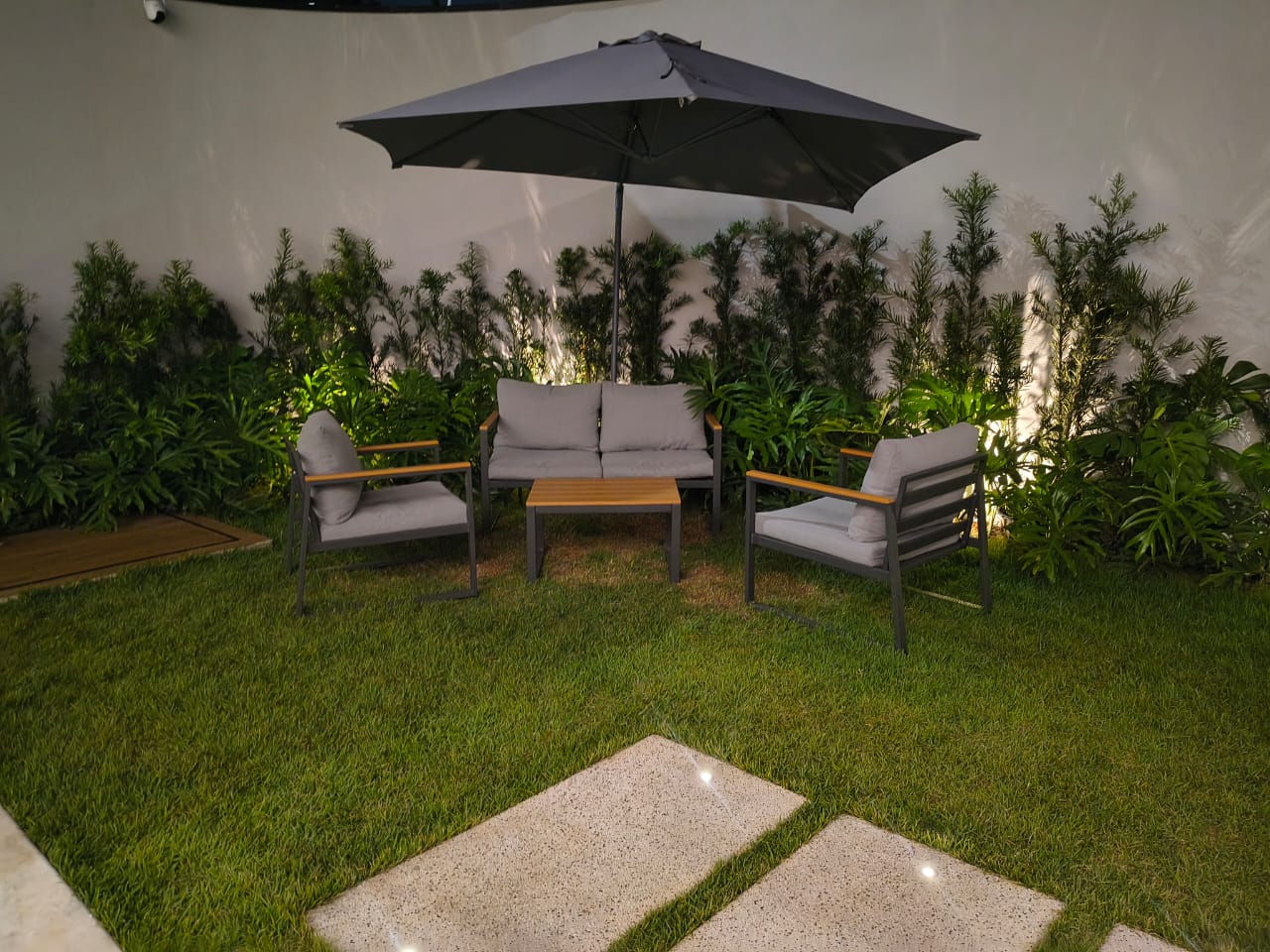 Lounge externo com sofás cinza, mesa de madeira e ombrelone preto
