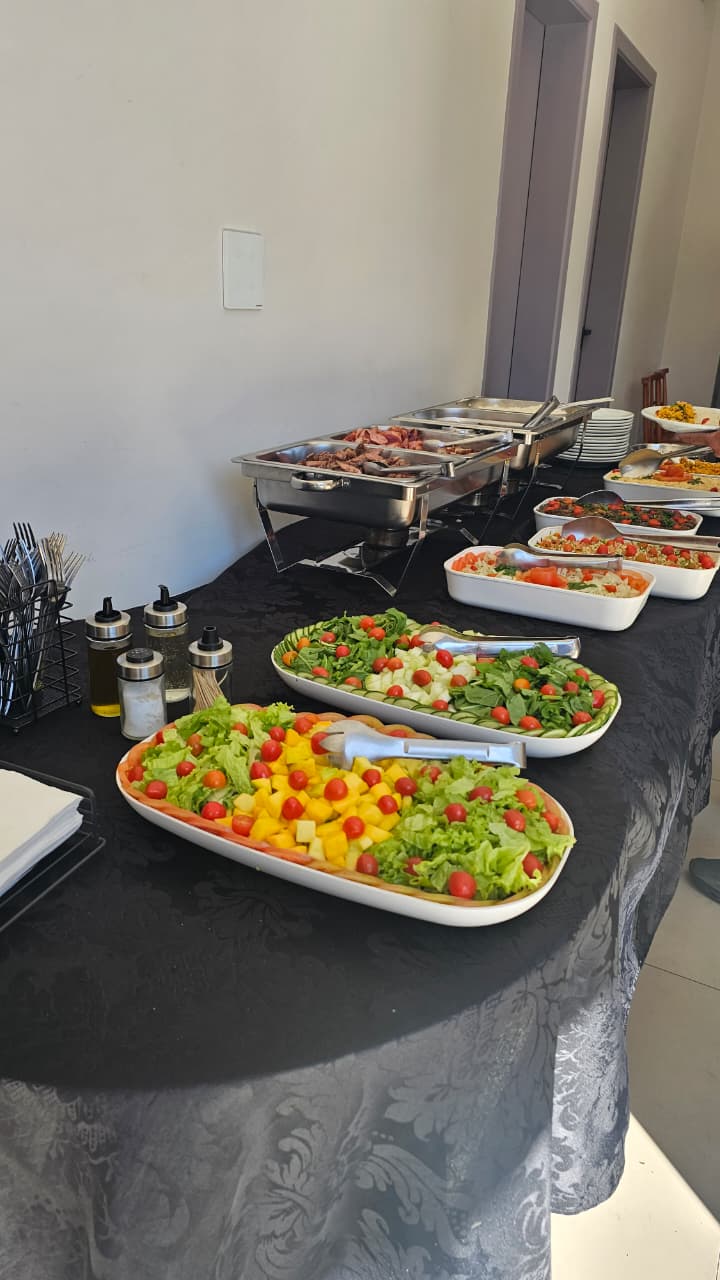 Buffet corporativo com saladas, réchauds e travessas em mesa preta